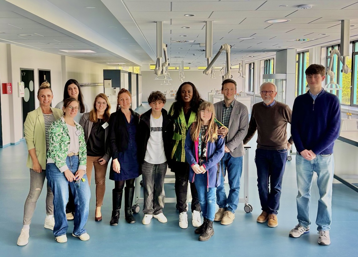 Gruppenfoto im hochmodernen, lichtdurchfluteten Naturwissenschafts-Raum (NTW) der IGS Gehrden. Die Landtagsabgeordnete Djenabou Diallo Hartmann steht lächelnd in der Mitte einer Gruppe von etwa zehn Personen, darunter Schüler*innen, Lehrkräfte und die Grünen Gehrden Vertreter Heinz Straßmann und Lisa Benda. Im Hintergrund sind moderne Laboreinrichtungen und flexible Deckenanschlüsse zu sehen. Das Bild symbolisiert Zukunft und Fortschritt in der Bildung.