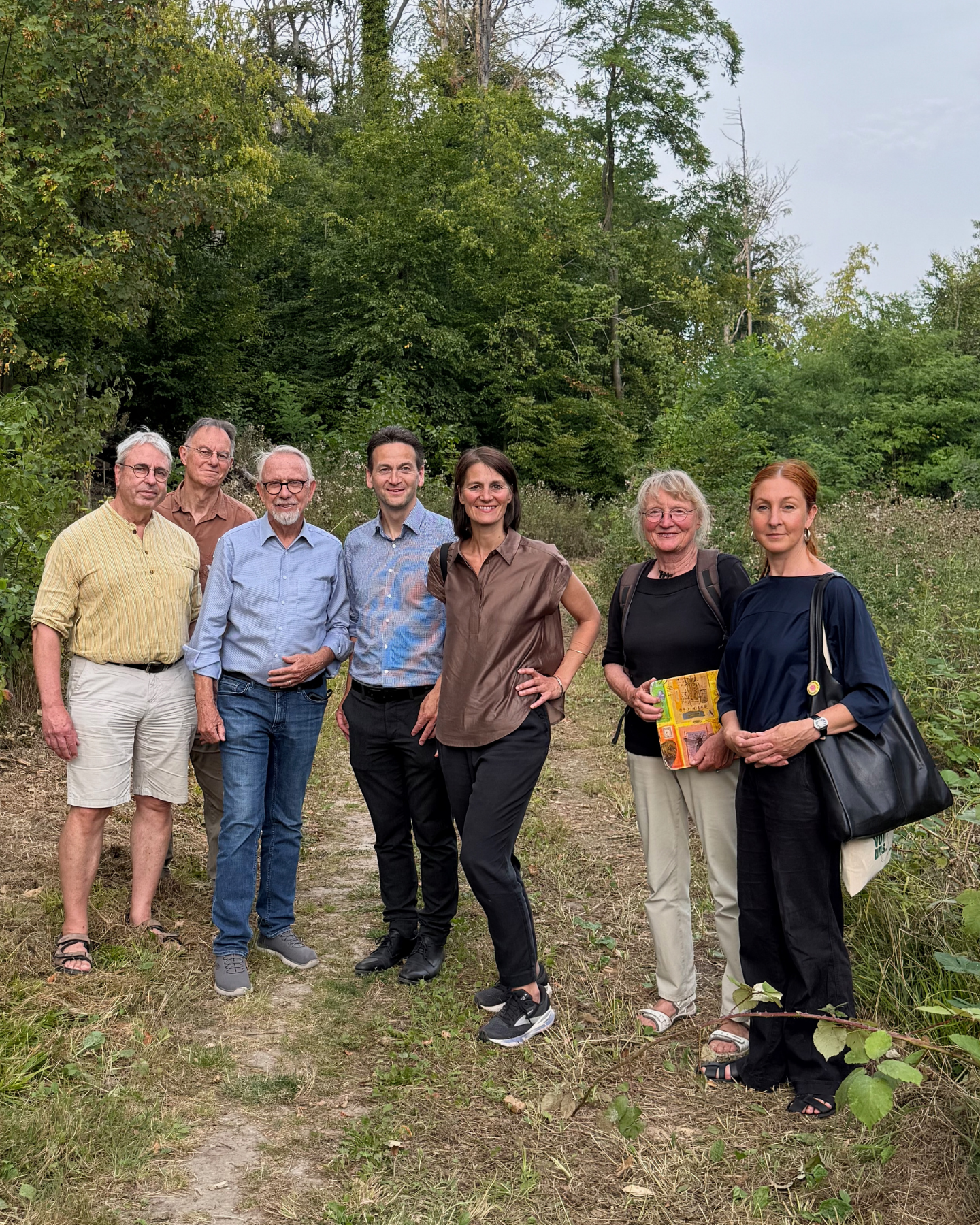 Gruppe von sieben Personen steht auf einem Waldweg vor dichtem Grün